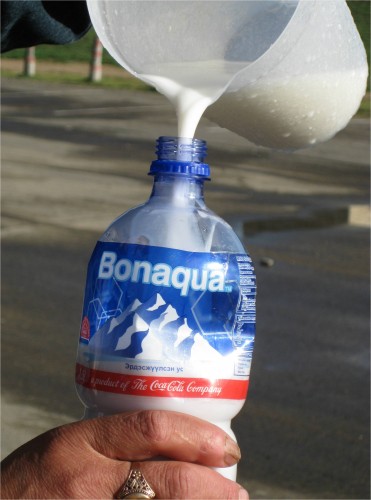 A woman pours airag into a recently used water bottle. Plastic 1.5 Litre water and cola bottles are the default storage containers for milk. Airag in the country is cheaper, costing just over a dollar per gallon.