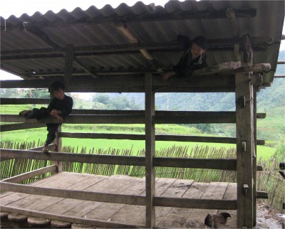A couple kids playing near the side of a tiny mountain road, near a tiny village.