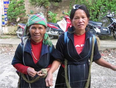 These H'Mong women work throughout the day, making clothing, while also selling them. They work the thread on their long walks into town, all while carrying bagpacks full of products for sale. Behind them are motorcycles for rent, and a sign for hairdressing, shave, and massage.